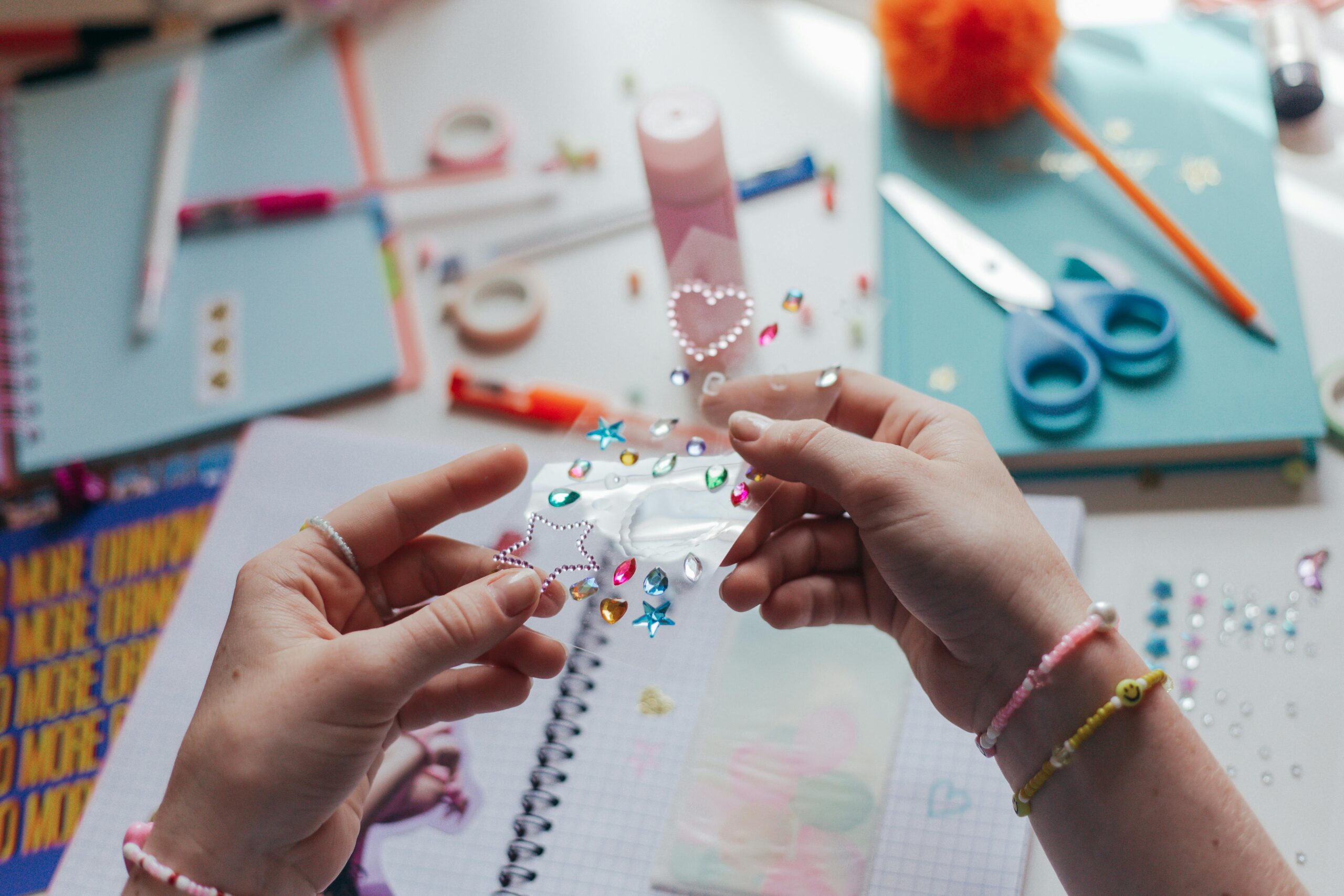 Hands decorating a notebook with colorful stickers in a creative workspace.